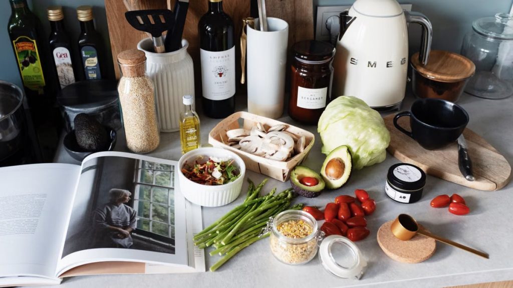 Various colorful healthy food and vegetables locating on countertop next to many different utensils and white kettle during cooking in stylish kitchen