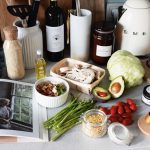 Various colorful healthy food and vegetables locating on countertop next to many different utensils and white kettle during cooking in stylish kitchen